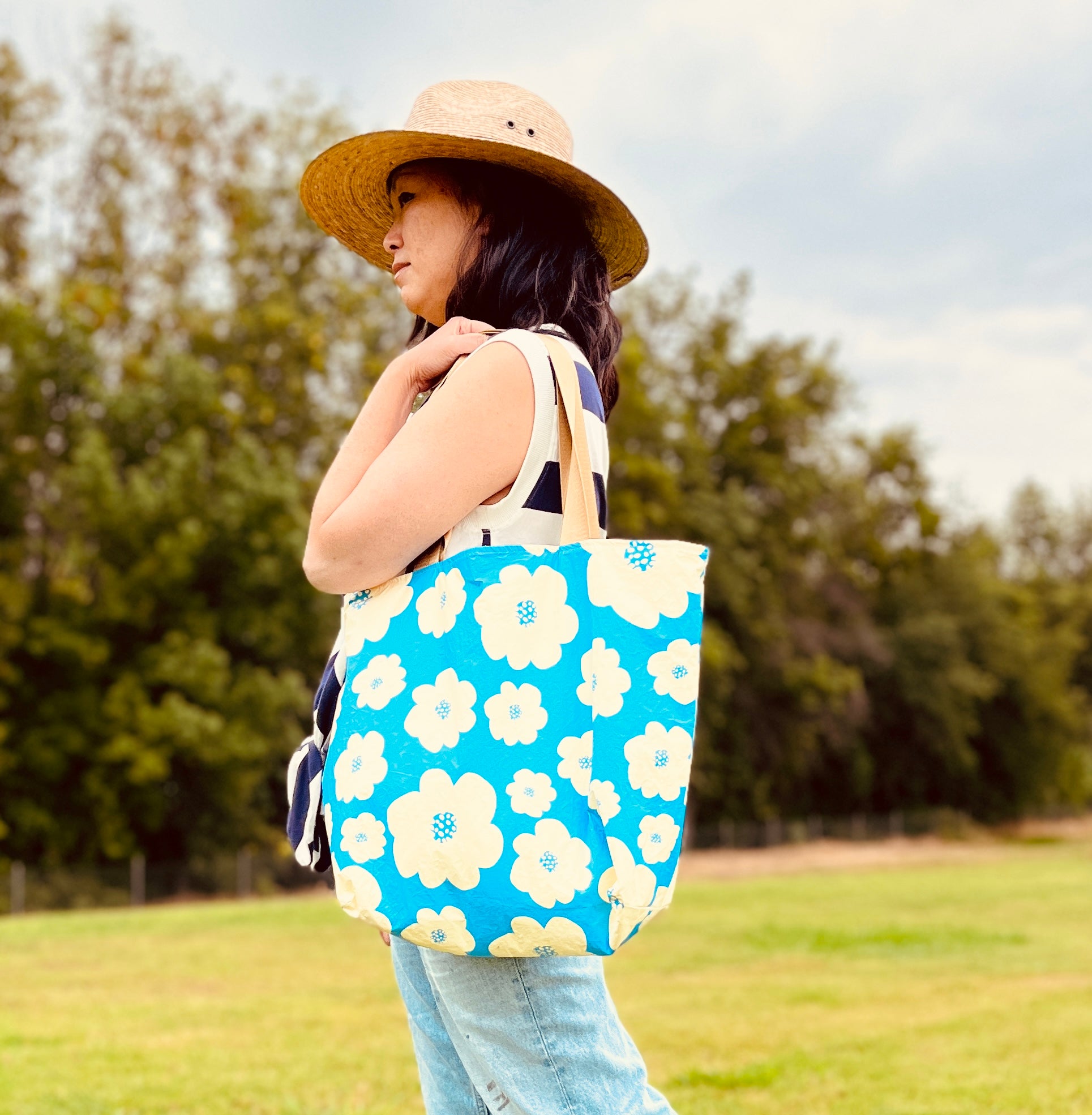 Woman holding the tote to show the size of the tote.  The bag falls mid torso and stops by the thigh.  Sturdy and waterproof bag great for everyday use.